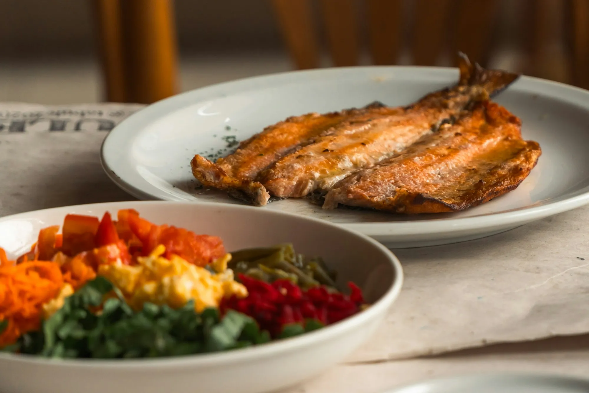 Peixe grelhado ao lado de um prato de salada colorida