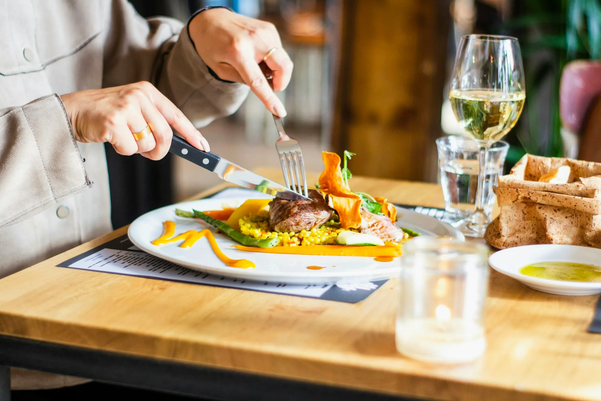 Pessoa cortando a comida num restaurante, com taças sobre a mesa